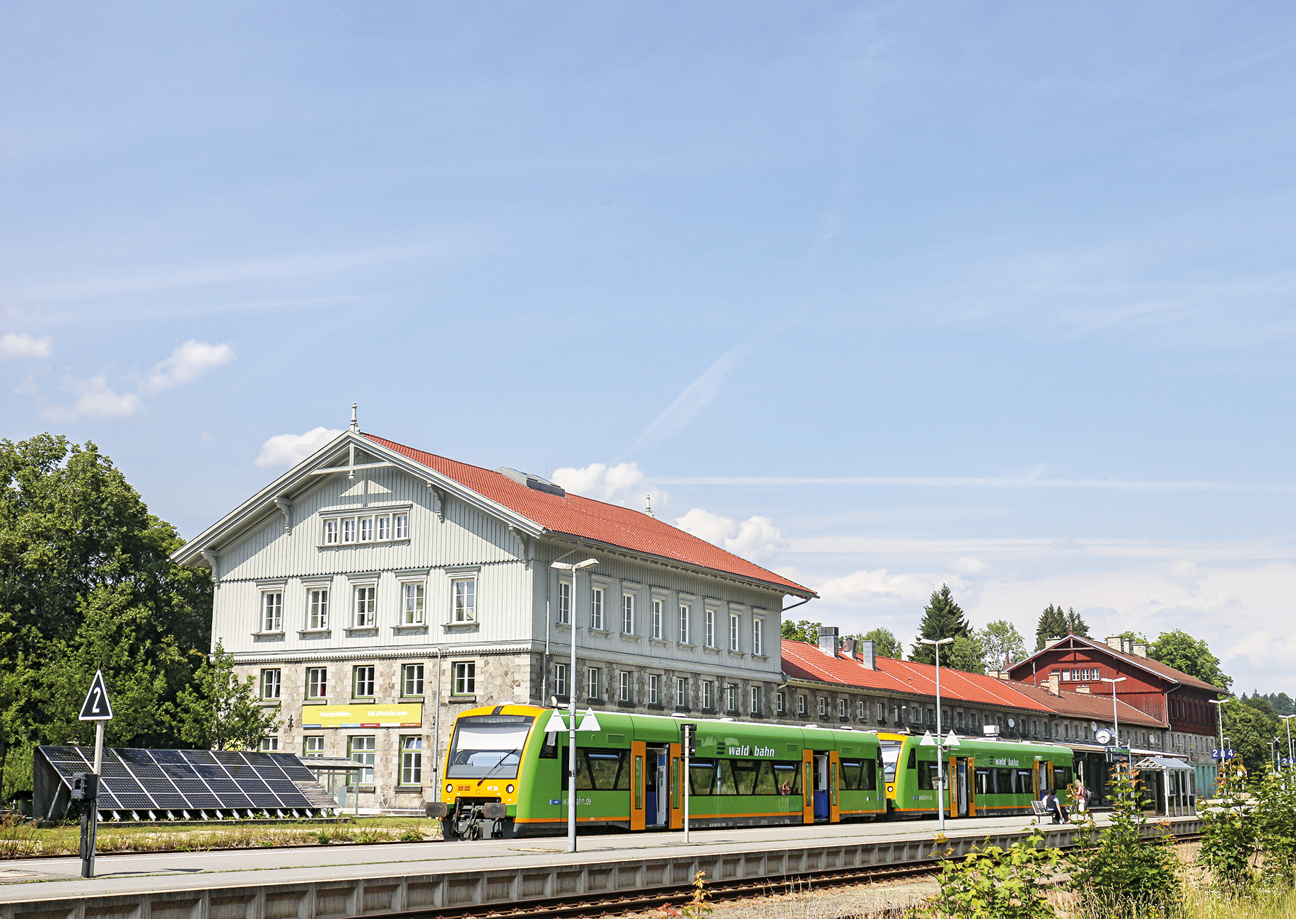 Bahnhofsgebäude, davor ein Regionalzug, seitlich eine Solaranlage
