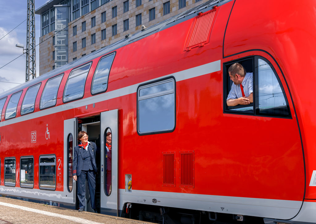 Kundenbetreuerin und Triebfahrzeugführer eines Regionalzugs am Bahnsteig im Gespräch