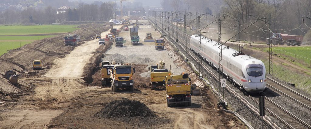 Baufahrzeuge neben einem Bahngleis mit ICE