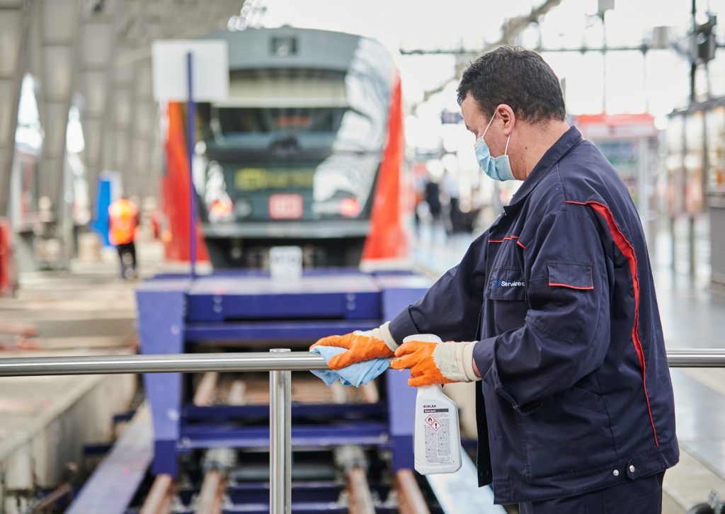 Mitarbeiter mit Mundschutz desinfiziert Geländer