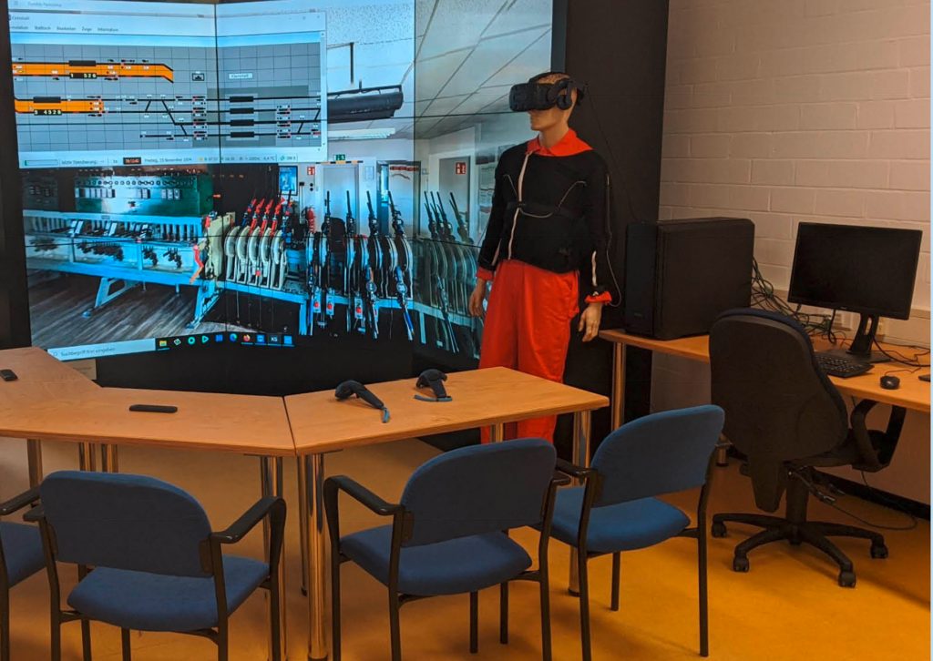 Menschliche Puppe mit VR-Brille vor einem Bildschirm mit Stellwerkssimulation
