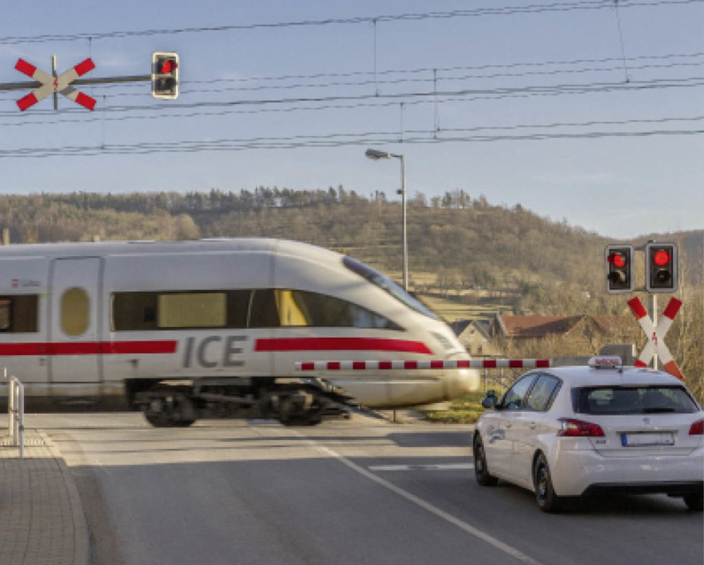 ICE fährt am geschlossenen Bahnübergang mit wartendem PKW