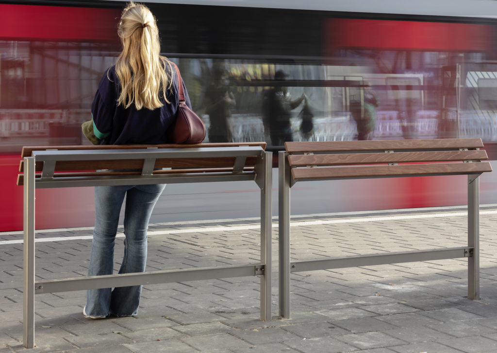 Frau am Bahnsteig an Stehhilfe, Zug fährt vorbei