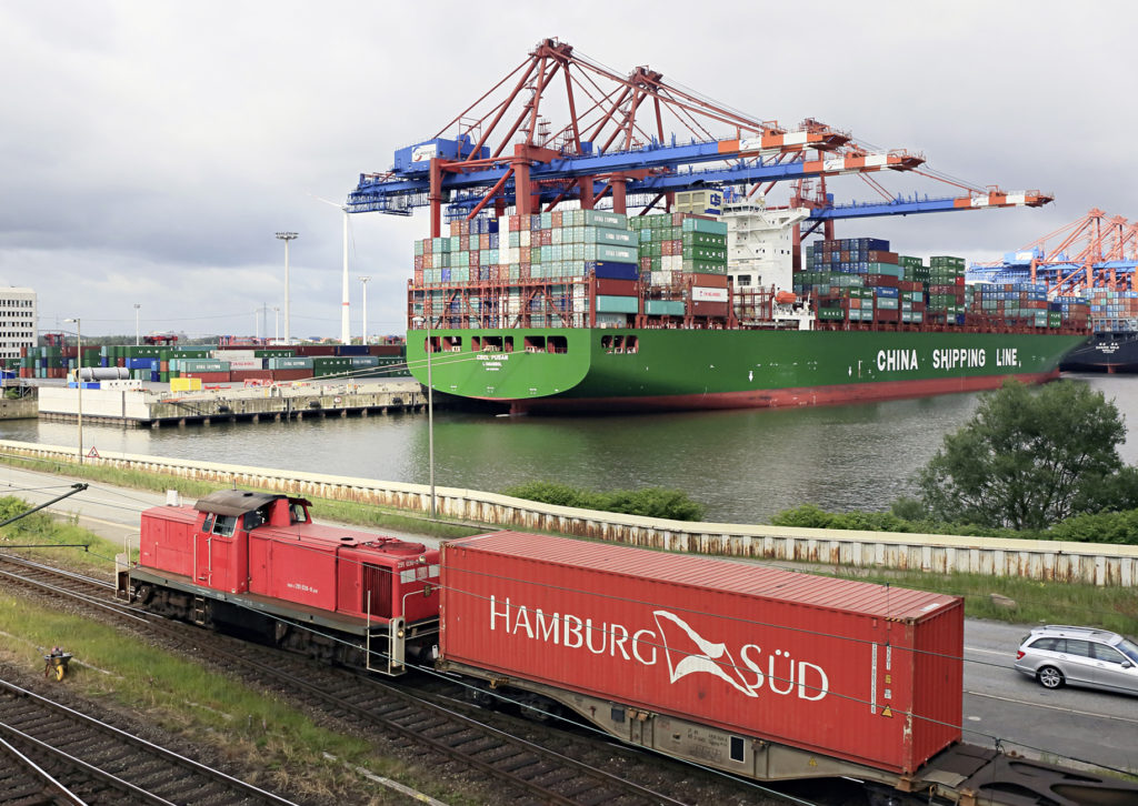 vorne Lok mit Container, auf dem Wasser großes Containerschiff