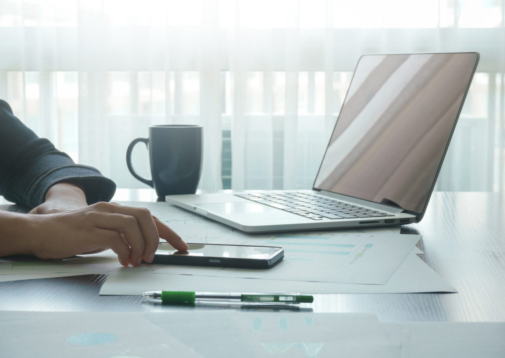 Person an Büro-Schreibtisch während der Arbeit mit Laptop und Smartphone