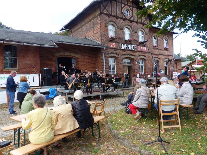 ein Orchester und Besucher vor Bahnhofsgebäude